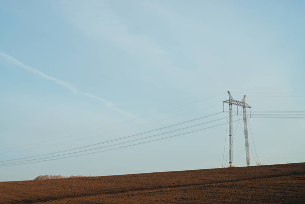 Atmospheric landscape with power lines in field under blue sky. Background image of electric tower with copy space. Wires of high voltage above ground. Electricity industry. - Photo, Image