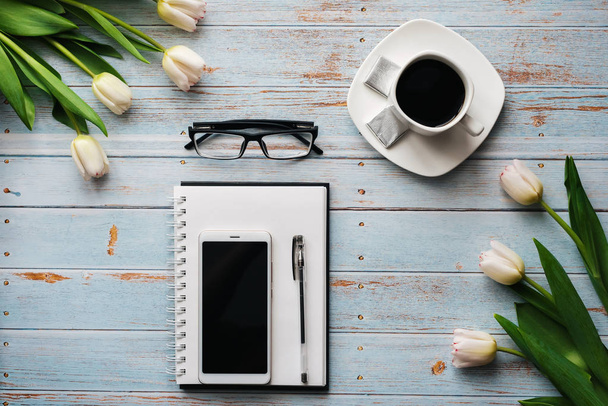 boeket van tulpen met een lege notebook, een kopje koffie en een smartphone op een houten achtergrond - Foto, afbeelding