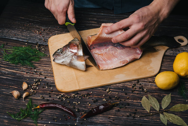 male chef cuts fresh red fish on a Board on a wooden table - Photo, Image