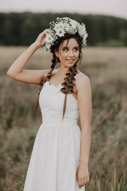 happy joyful girl with braids and a flower wreath in a white dress smiles - Photo, Image