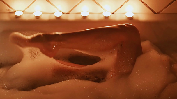 γυμνός μελαχρινή κορίτσι χαϊδεύει σεξουαλικά τα πόδια της και απολαμβάνει στο μπάνιο με αφρό με ένα ποτήρι σαμπάνιας - Πλάνα, βίντεο