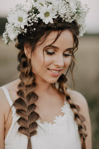 щаслива усміхнена дівчина з косами і квітковим вінком у білій сукні в стилі бохо влітку на відкритому повітрі
 - Фото, зображення