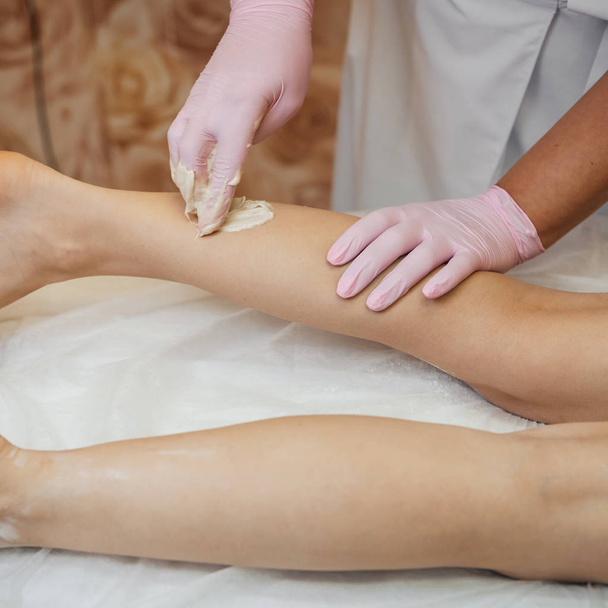 žena kosmetička provádí proceduru depilace cukru s medem na nohách ležící dívky - Fotografie, Obrázek