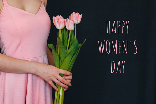 Blumenstrauß aus rosa Tulpen in den Händen eines Mädchens. Glückwunschkarte mit Text zum Frauentag - Foto, Bild