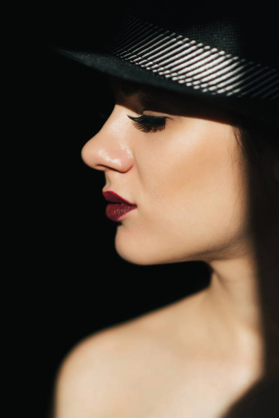 fashion portrait in profile of a young sexy girl in a black hat with red lipstick - Photo, image