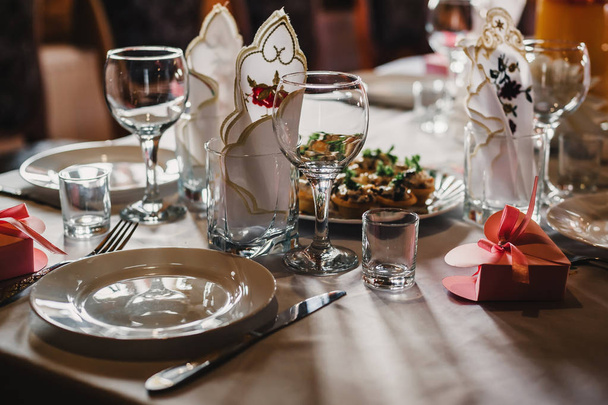 レストランのテーブルの上の白いテーブルクロスの上にカトラリーと空のメガネとプレートのセット - 写真・画像