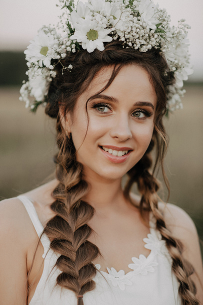 heureuse fille souriante avec des tresses et une couronne florale en robe blanche dans le style boho en été à l'extérieur
 - Photo, image