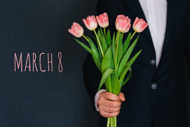 Мужчина дарит букет розовых цветов тюльпанов. Открытка с текстом 8 марта
 - Фото, изображение
