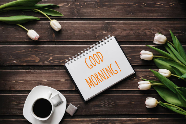 weiße Tulpenblüten mit einer Tasse Kaffee auf einem Holztisch. Grußkarte mit Schriftzug Guten Morgen - Foto, Bild