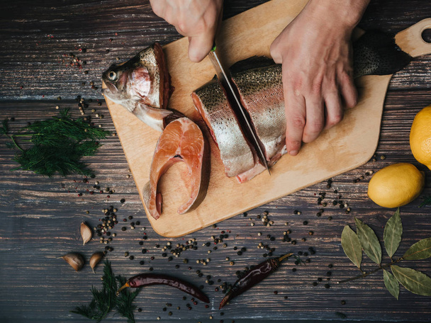 forel op het bord, die snijdt een man koken met een mes. Verse rauwe rode vis - Foto, afbeelding