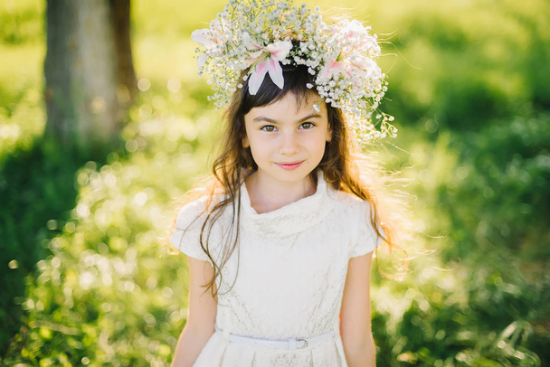Portret van een jong meisje met een krans van bloemen op haar hoofd op een weide - Foto, afbeelding