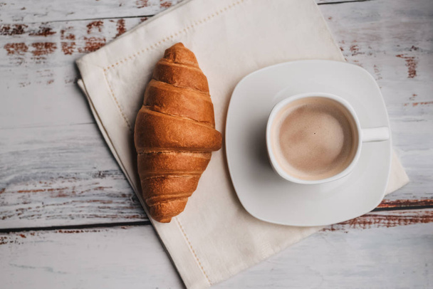 Manhã Café da manhã de croissant e café em uma xícara branca em uma mesa de madeira
 - Foto, Imagem