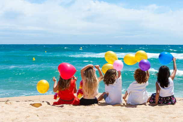 Enfants assis sur la plage avec des ballons de couleur
. - Photo, image