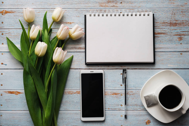 Wit boeket tulpen op houten achtergrond met koffiekopje, smartphone en lege notebook - Foto, afbeelding