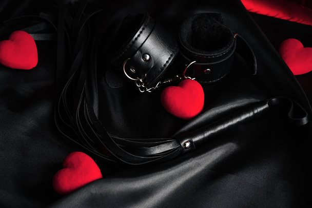 Látigo de cuero y esposas para el sexo BDSM con corazones rojos como símbolo del día de San Valentín
 - Foto, Imagen