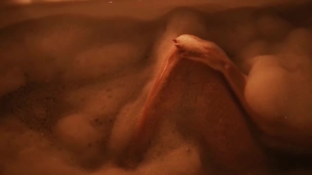 nackte brünette Mädchen streichelt sexuell ihre Beine und genießt im Badezimmer mit Schaum ein Glas Champagner - Filmmaterial, Video
