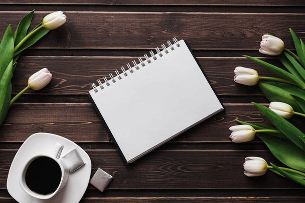 White tulips on a wooden table with a Cup of coffee and an empty notebook - Photo, Image