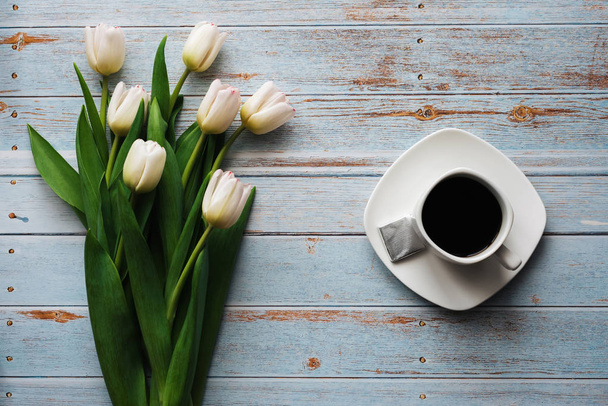 Wit boeket tulpen op een houten blauwe achtergrond met een kopje koffie - Foto, afbeelding