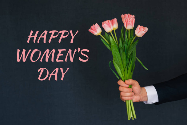 Vaaleanpunaisia tulppaaneja miehen kädessä. Onnittelukortti tekstin kanssa Hyvää naistenpäivää
 - Valokuva, kuva