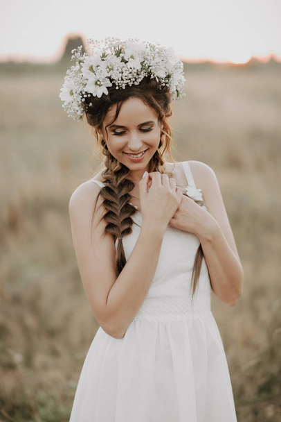 happy smiling girl with braids and floral wreath in white dress in boho style in summer outdoors - Zdjęcie, obraz