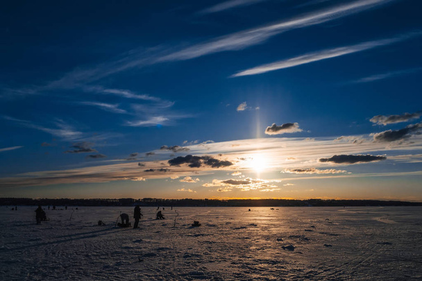 Zimowy połów. Sylwetka rybaków łowiących ryby na lodowatej powierzchni rzeki w tle piękny wschód słońca - Zdjęcie, obraz