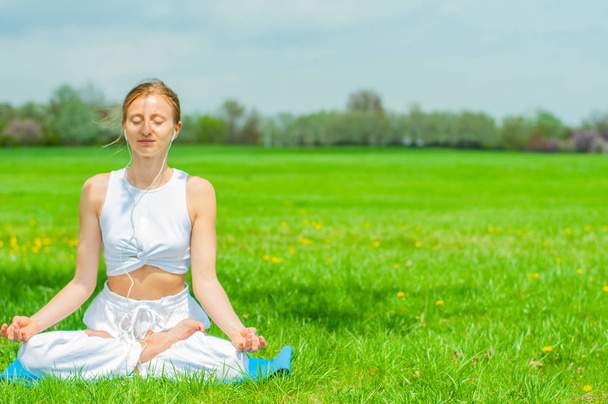 Beautiful woman is practicing yoga sitting in Lotus pose on grass - Photo, Image