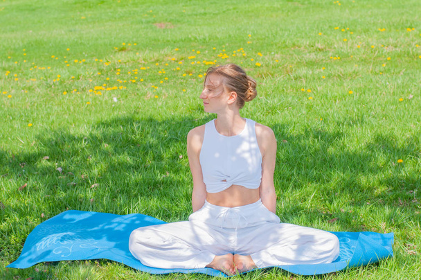 Beautiful woman is practicing yoga sitting in Lotus pose on grass - Photo, Image