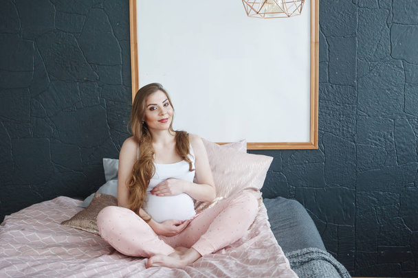 Boldog terhes nő ül az ágyon otthon - Fotó, kép
