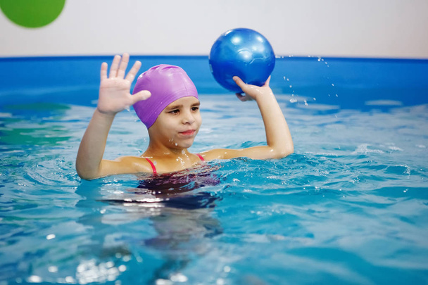 Menina no chapéu lilás está se divertindo, nadando na piscina
. - Foto, Imagem