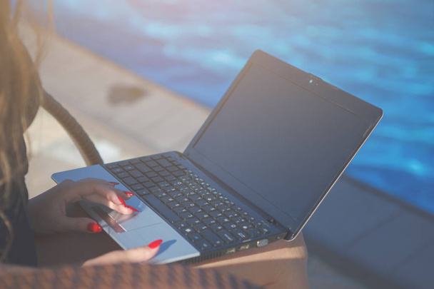 Jovem mulher bonita está trabalhando com um laptop perto de uma piscina com azul
  - Foto, Imagem
