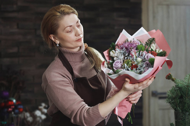 Девушка-флористка в коричневом фартуке показывает покупателю красивый бутик
 - Фото, изображение
