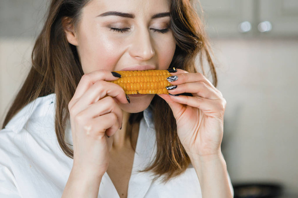 Młoda kobieta jedzenia gotowanej kukurydzy. - Zdjęcie, obraz