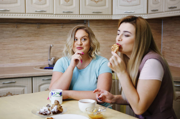 Two girlfriends women in the kitchen are having fun and eating food. - Photo, Image