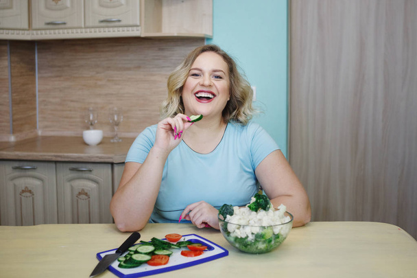 Mladá docela Tlustá blondýna žena jíst zelené okurky a brokolice. Pojem zdravé jídlo, strava, boj proti obezitě. - Fotografie, Obrázek