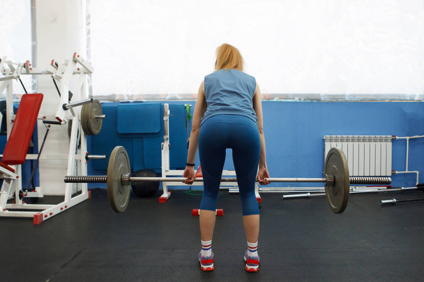 Young athletic woman raises the sport barbell in the gym. - Photo, Image