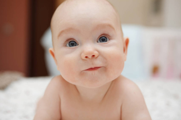 Hermosa bebé de cinco meses de ojos azules niña acostada sobre su estómago, varias emociones en su cara. Mirada infantil. Cuidado materno. Cuidado de niños. Primer plano
. - Foto, imagen