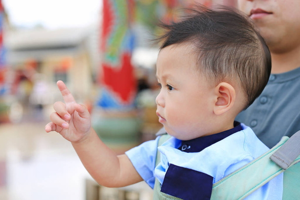 Adorable little baby boy pointing something with father carry by hipseat outdoor. Close up. - Fotó, kép