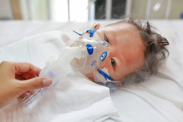 Sick baby boy applying inhale medication by inhalation mask to cure Respiratory Syncytial Virus (RSV) on patient bed at hospital. - Photo, image