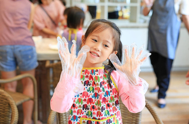 Little Chef wearing transparent plastic gloves in hands while cooking in the kitchen. - Fotó, kép