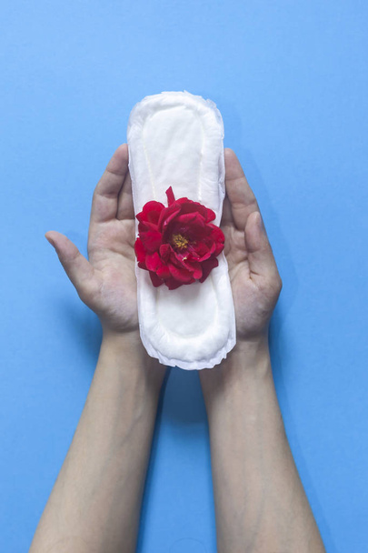 Female's hand holding sanitary napkins with red rose on it. Period days concept showing feminine menstrual cycle. Female's hygiene - Foto, Imagem