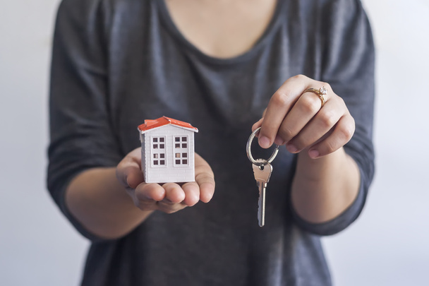 Woman holding miniature toy house and keys. Real estate agent holding keys and toy house. Buying or selling real estate - 写真・画像