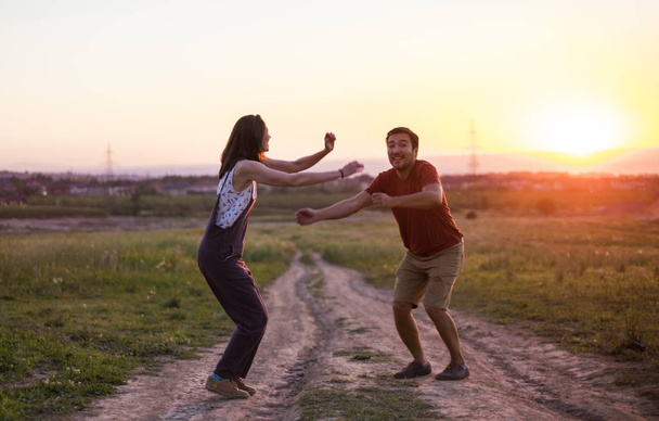 happy couple man and woman dancing on the country road at the beautiful sunset - Photo, image