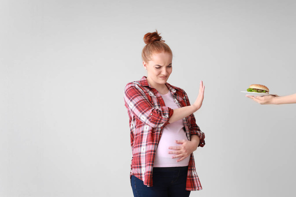 Young pregnant woman refusing to eat tasty burger on light background - Foto, Imagem