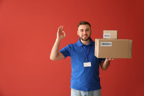 Handsome delivery man showing OK on color background - Photo, Image