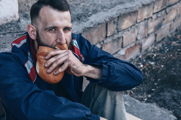 Бедный бездомный ест хлеб на открытом воздухе
 - Фото, изображение