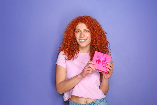 Beautiful redhead woman with gift on color background - Foto, Bild