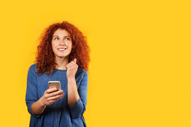 Ajattelevainen punapää nainen matkapuhelimella värillä taustalla
 - Valokuva, kuva