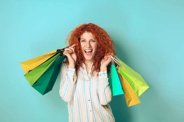 Beautiful redhead woman with shopping bags on color background - Фото, зображення