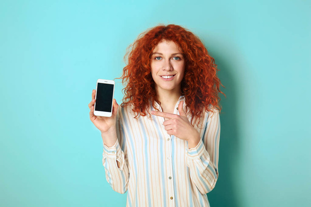 Gyönyörű vöröshajú nő, mobiltelefonnal a színes háttér - Fotó, kép