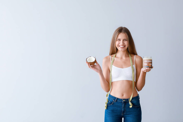 Красивая молодая женщина с банкой кокосового масла и измерительной лентой на светлом фоне. Концепция потери веса
 - Фото, изображение